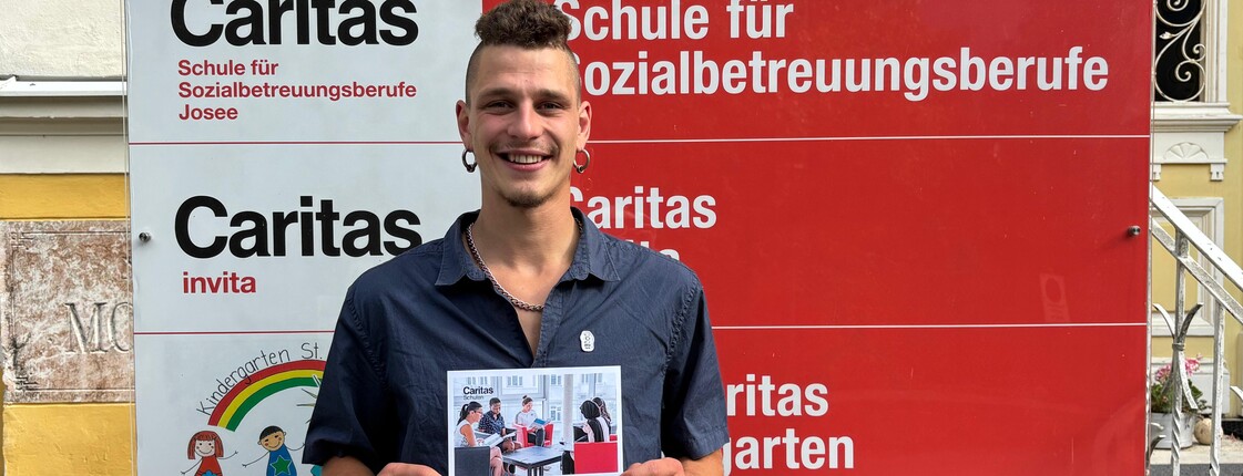 Junger Mann lächelt und hält eine Urkunde in die Kamera.